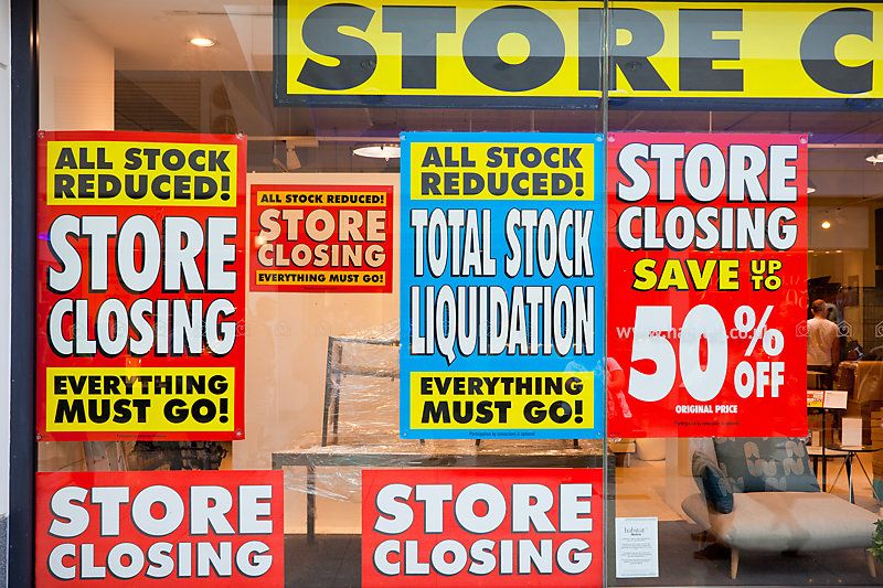 View of a diplay window of a furniture store with posters of total stock liquidation and big discounts due the imminent closure.