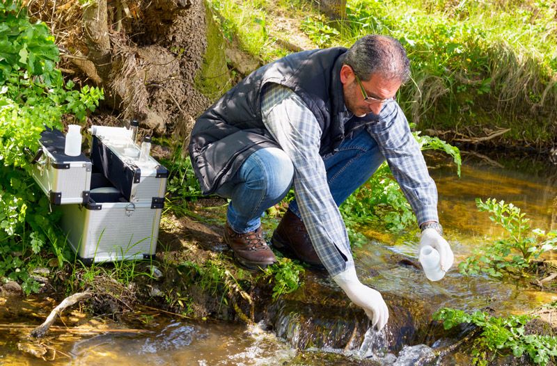 A biologist takes a water sample in a river