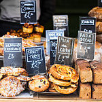 Selection of pastries and bread on bakery stall at a food market, with price labels.