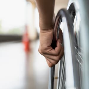 Close-up of a disabled man's hand, holding the wheel of his wheelchair.