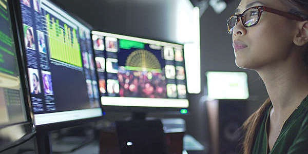 Close-up of a young woman at work in front of three computer screens.