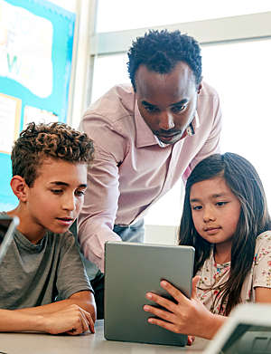 Teacher helps school children using a tablet in the classroom.