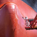 A worker spray painting the underside of a ship in dry dock.