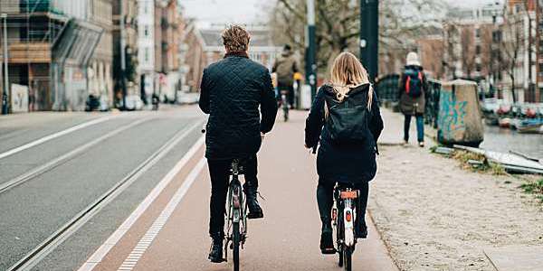 Back view of a man and a woman cycling next to each other on a city cycle path.