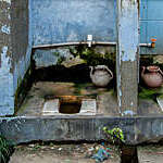Two dilapidated open-air squatting toilets with scaling blue-painted walls.