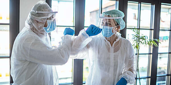 Two doctors wearing full body and face protection against COVID-19 bump elbows in greeting.