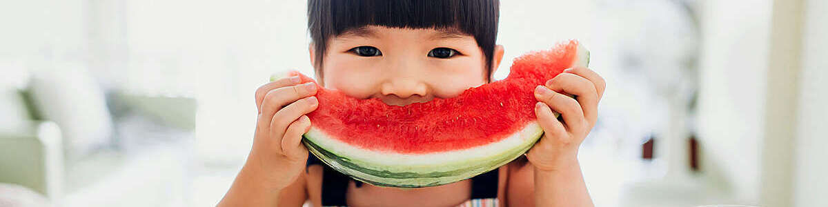 Asian little girl eating a slice of watermelon at home.