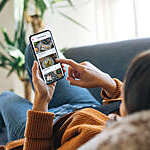 Over the shoulder view of a young woman choosing food from the menu on mobile app while lying on the couch at home.